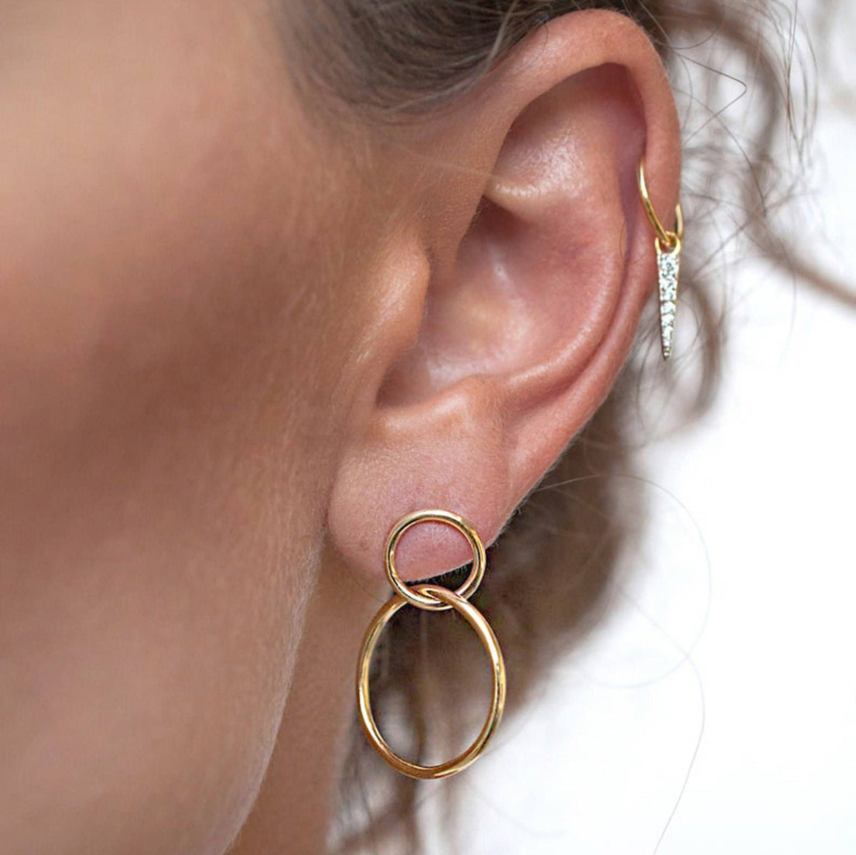 Close up of a woman wearing a 14k gold plated Sena double circle stud hoop earring