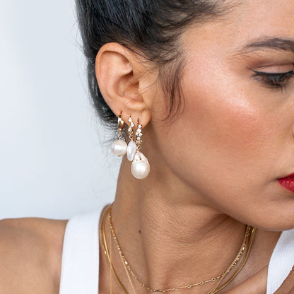 Close up side view of a woman wearing 14k gold filled Amia baroque pearl drop earrings
