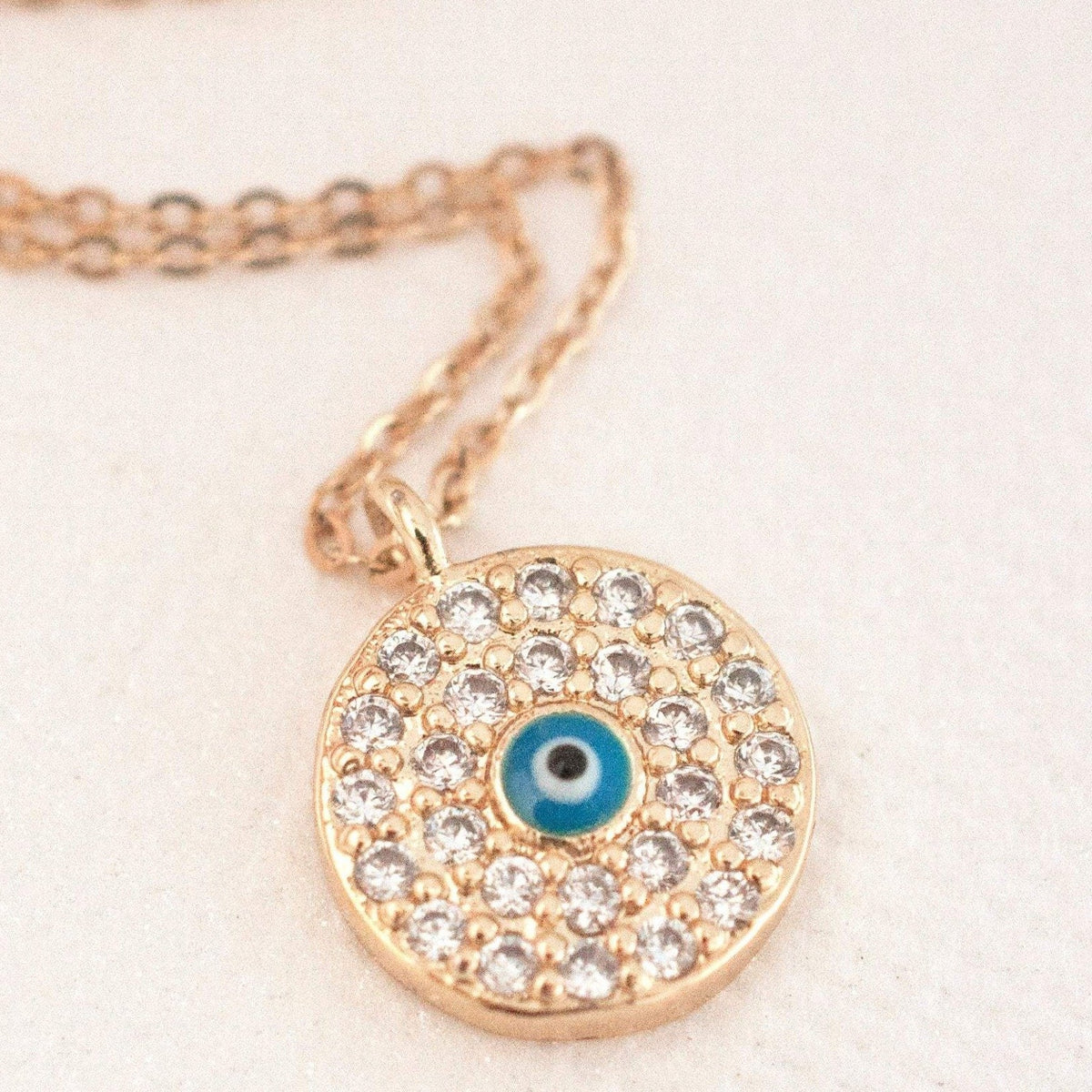 Elin Round Evil Eye 14k gold filled round medallion pendant with clear cz pave surround and blue enamel eye on soft fabric