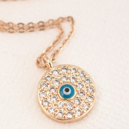 Elin Round Evil Eye 14k gold filled round medallion pendant with clear cz pave surround and blue enamel eye on soft fabric