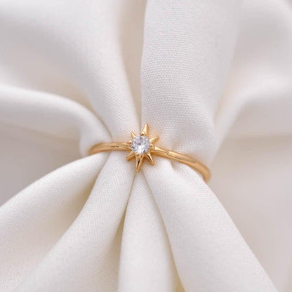 Gold starburst ring with a clear crystal solitaire on white draped fabric.