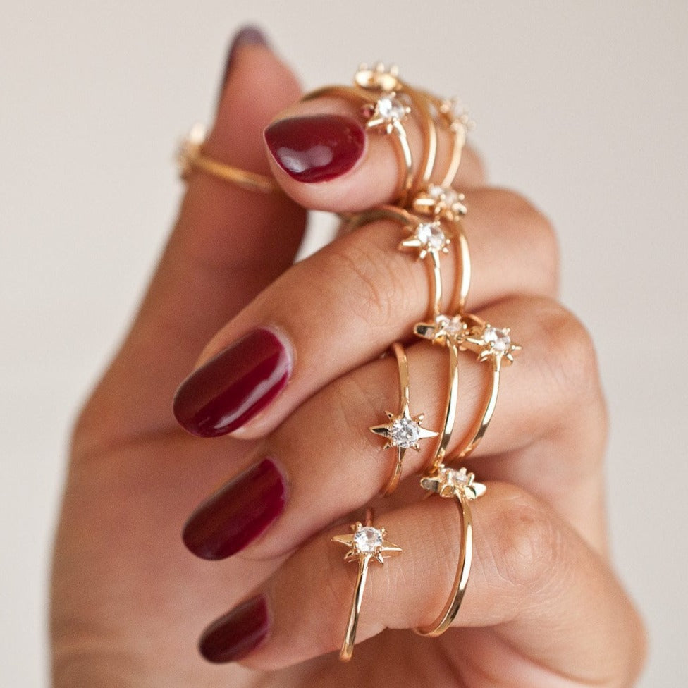 Hand with dark red nails holding a stack of thin gold starburst rings.