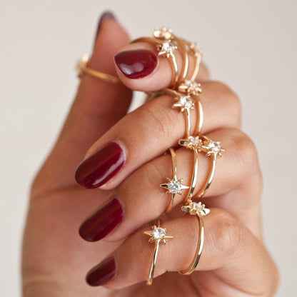 Hand with dark red nails holding a stack of thin gold starburst rings.
