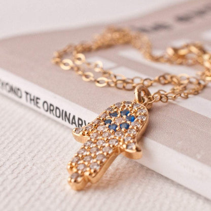 Macro detail of Asha Hamsa Hand 14k gold filled necklace displayed flat on white surface