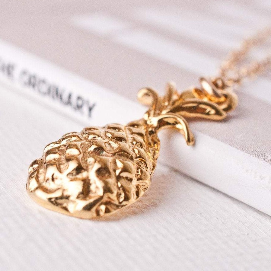 Macro detail of Copia Pineapple Goddess 14k gold filled textured pineapple pendant resting on white surface