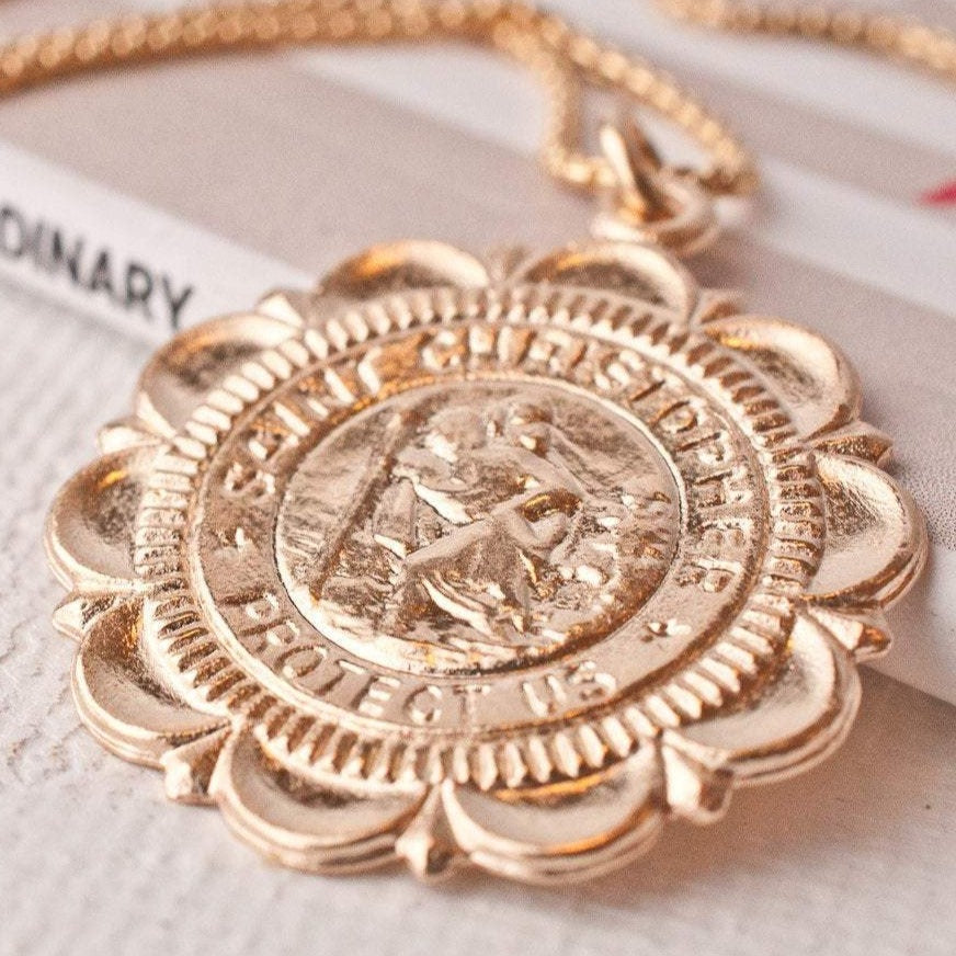 Macro detail of Viva Saint Christopher 14k gold filled scalloped edge coin pendant resting on white surface