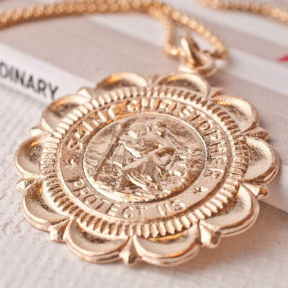 Macro detail of Viva Saint Christopher 14k gold filled scalloped edge coin pendant resting on white surface
