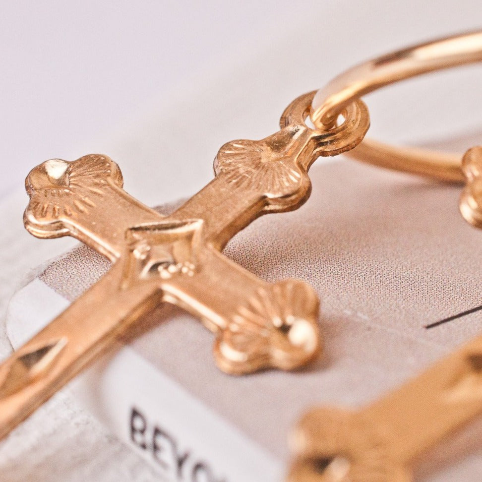 Macro view of the detailed cross charm on a 14k gold filled Haven hoop earring