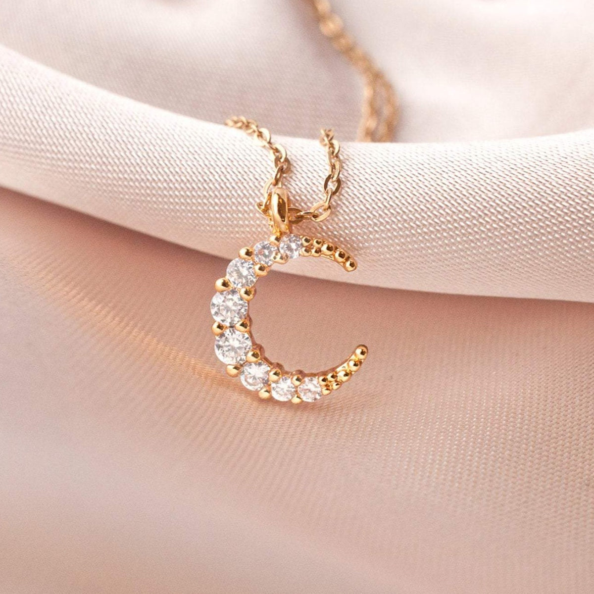 Maja Mini Moon 14k gold filled crescent pendant with cz crystals resting on soft pink fabric