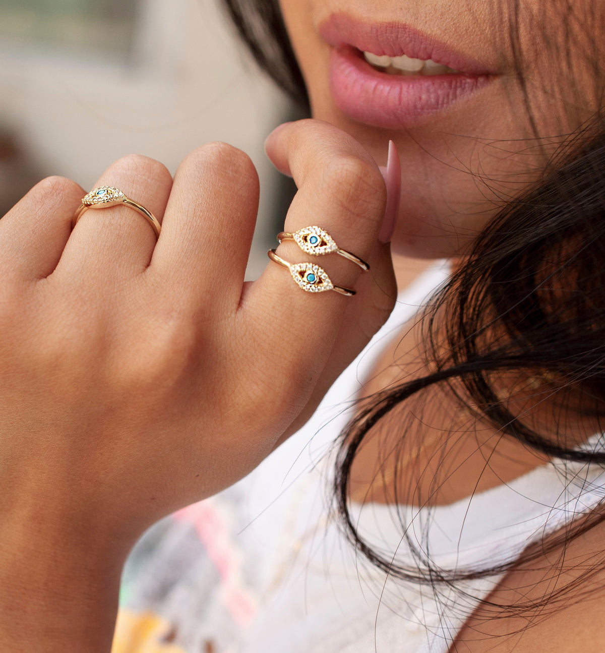 Model wearing stacked gold evil eye rings featuring pavé diamonds and turquoise center stones.