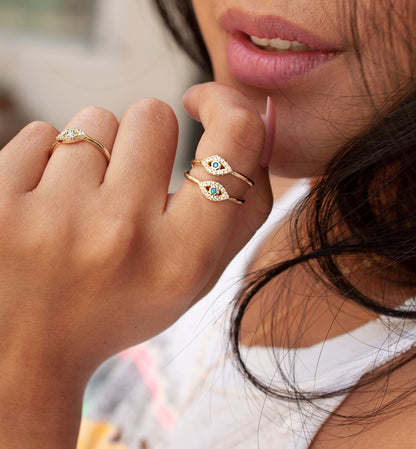 Model wearing stacked gold evil eye rings featuring pavé diamonds and turquoise center stones.