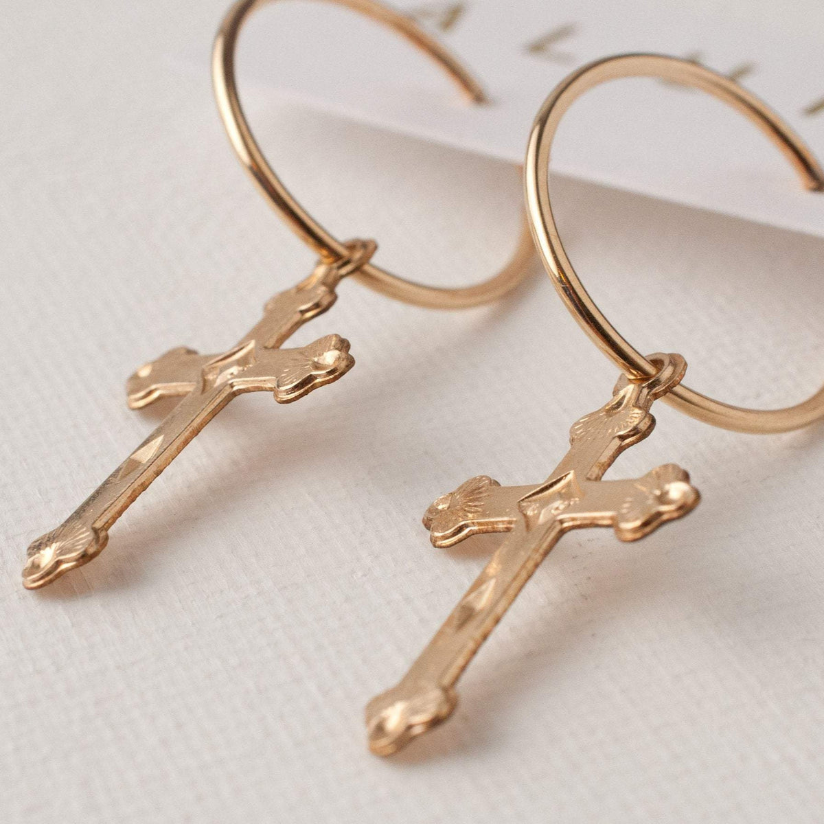 Pair of 14k gold filled Haven cross charm hoop earrings lying flat
