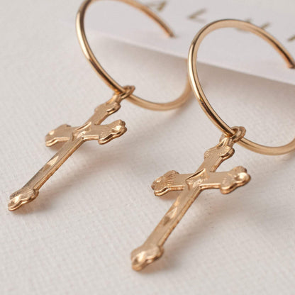 Pair of 14k gold filled Haven cross charm hoop earrings lying flat