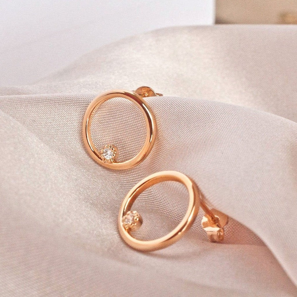 Pair of Ora Circle Solitaire 14k gold plated earrings on white fabric