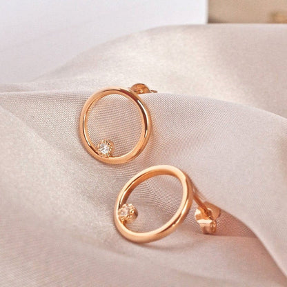 Pair of Ora Circle Solitaire 14k gold plated earrings on white fabric