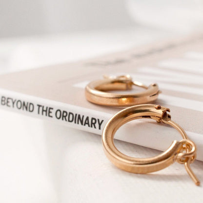 Pair of women's 14k Gold Filled Zola Hoop Earrings resting flat on a open book.