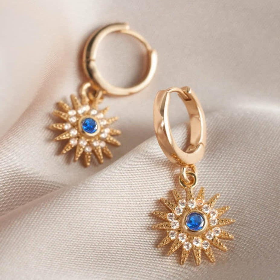 Pair of women's 14k Gold Plated Astrid Starburst Earrings resting on soft silk fabric.