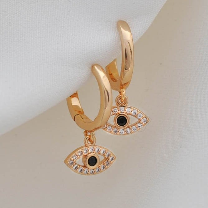 Pair of women's 14k Gold Plated Mira Evil Eye hoop earrings with crystal pavé dangles hanging on a smooth surface.