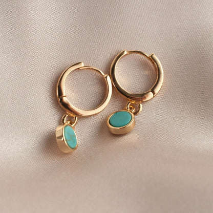 Pair of women's 14k Gold Plated Riva Turquoise Charm Hoop Earrings resting flat on soft beige satin cloth.