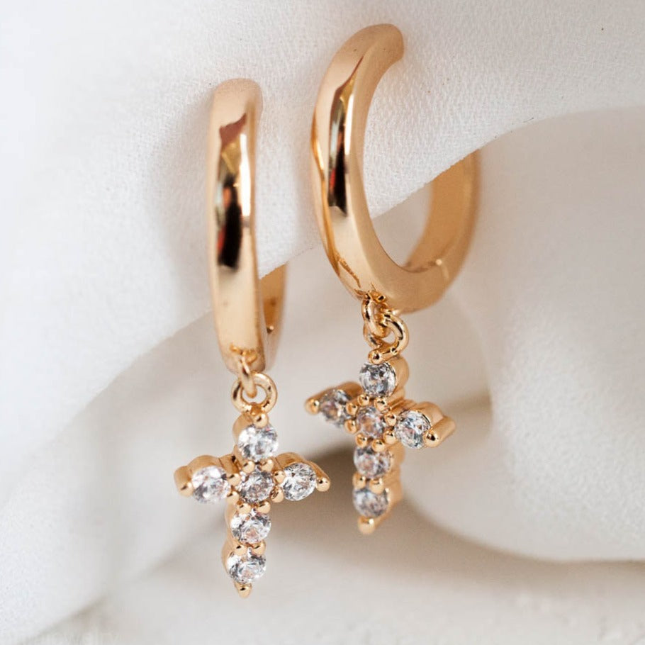 Pair of women's 14k Gold Plated Solid Mini Cross Hoops with crystal accents draped over white satin cloth.