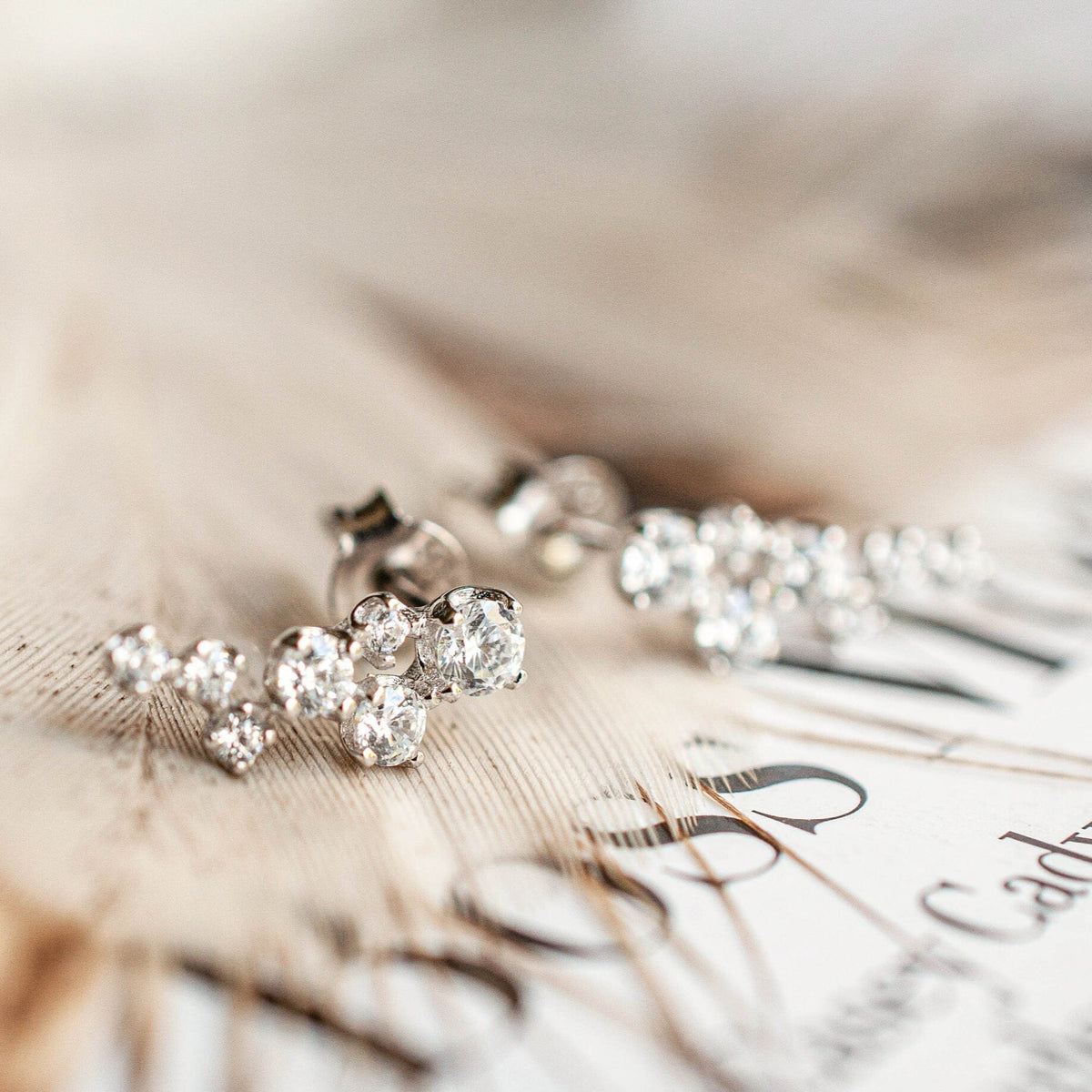 Pair of women's Sterling Silver Freja Ear Climbers resting flat on printed paper with feather accents.