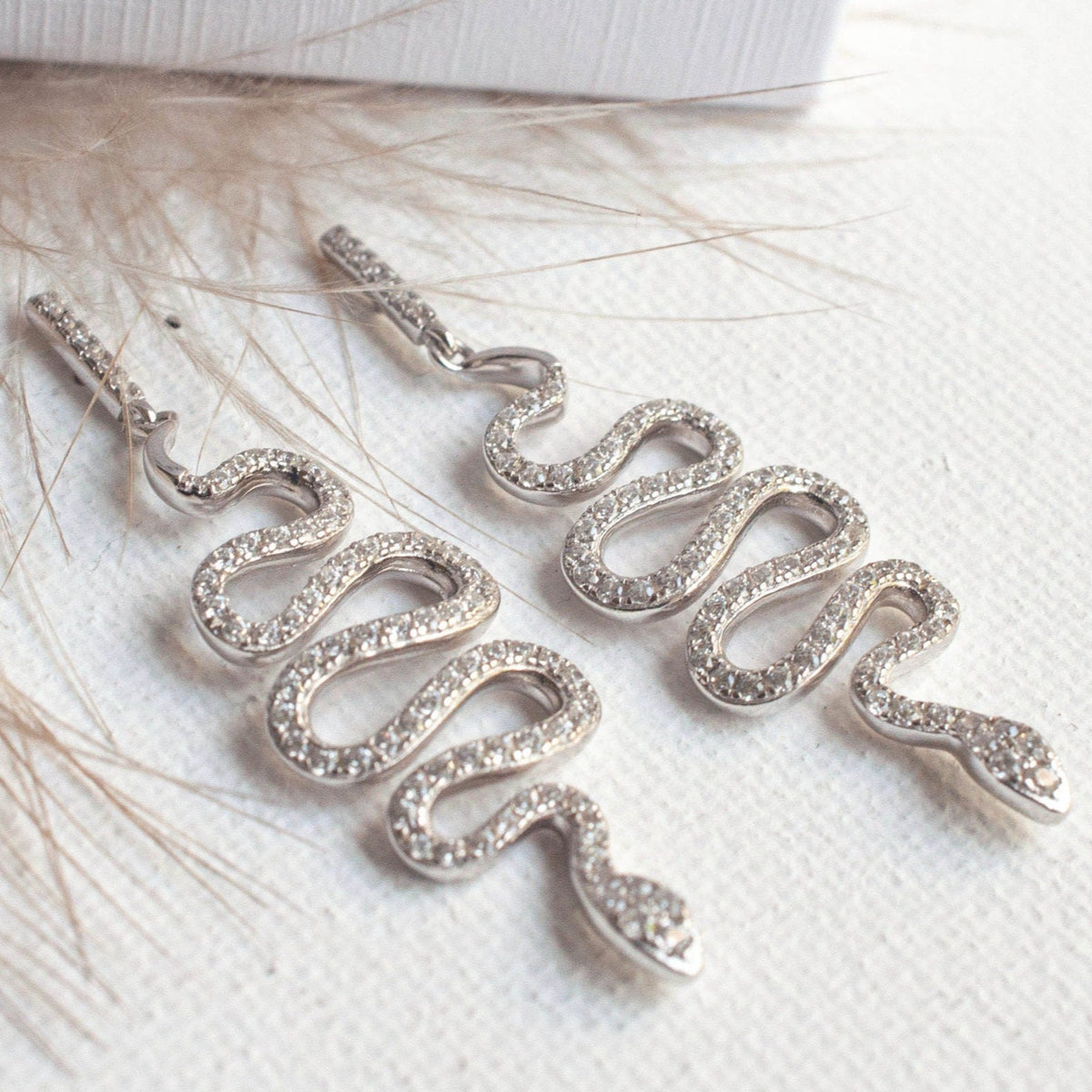 Pair of women's Sterling Silver Vivia Snake Earrings laid out on a textured white fabric surface.