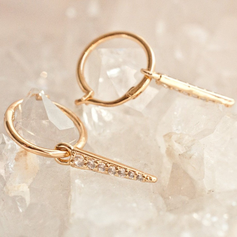 Pair of women's gold-plated hoop earrings with crystal spike dangles resting on a crystal rock background.