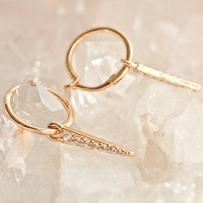 Pair of women's gold-plated hoop earrings with crystal spike dangles resting on a crystal rock background.