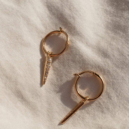 Pair of women's gold Plated  hoop earrings with spike pendant charms on textured fabric.