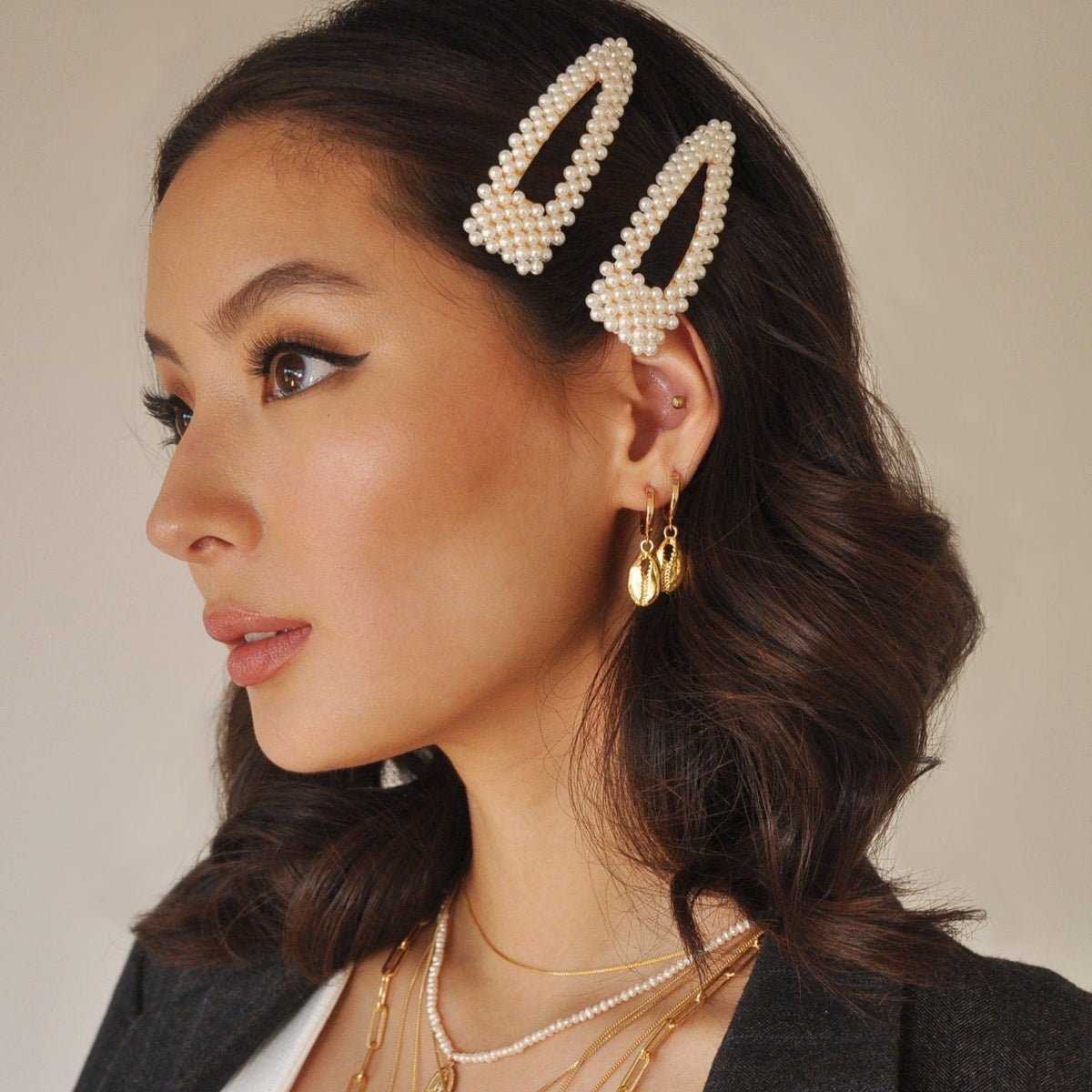 Side profile of a dark-haired woman wearing hair clips and a 14k Gold Plated Dola Seashell Earring with gold necklaces.