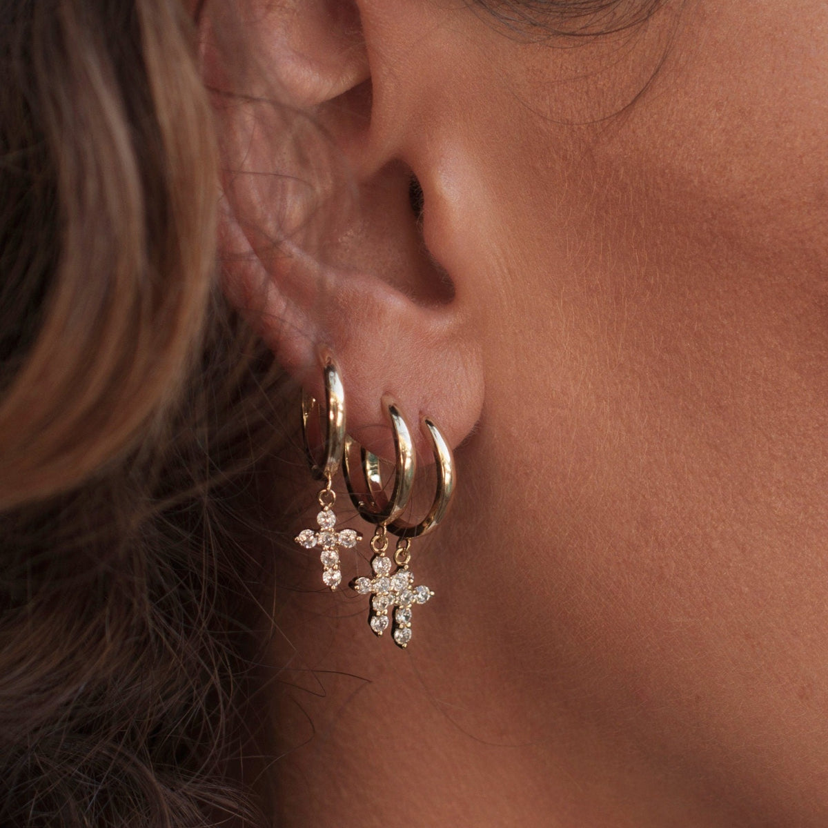 Side profile view of a woman wearing stacked 14k Gold Plated Solid Mini Cross Hoops.
