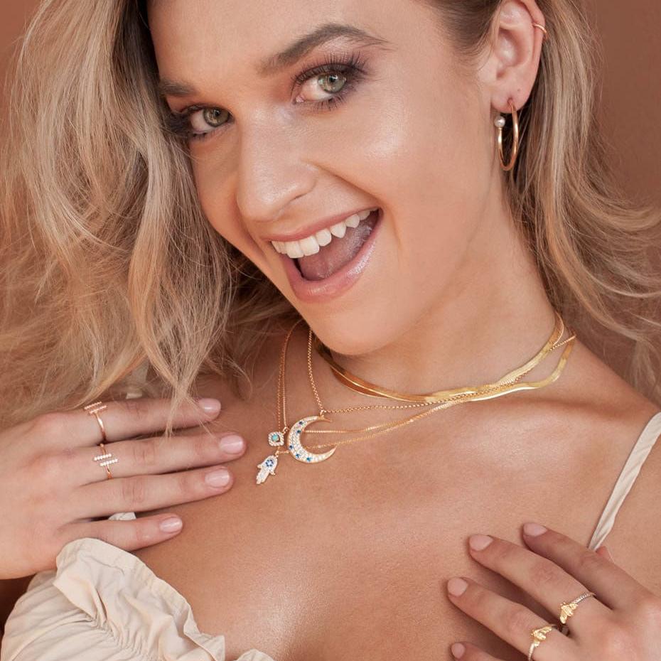 Smiling blonde woman wearing Elara Moon 14k gold filled crescent necklace holding hands near collarbone