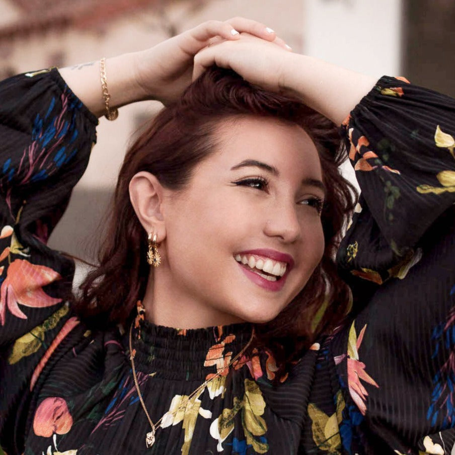 Smiling woman with hands in her hair wearing 14k Gold Plated Astrid Starburst Earrings and a floral top.