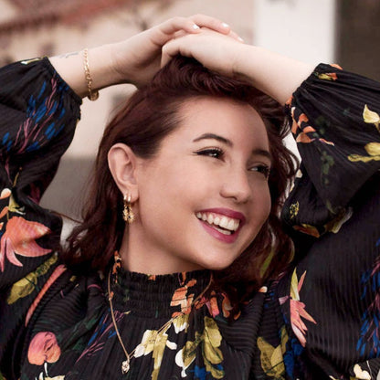 Smiling woman with hands in her hair wearing 14k Gold Plated Astrid Starburst Earrings and a floral top.