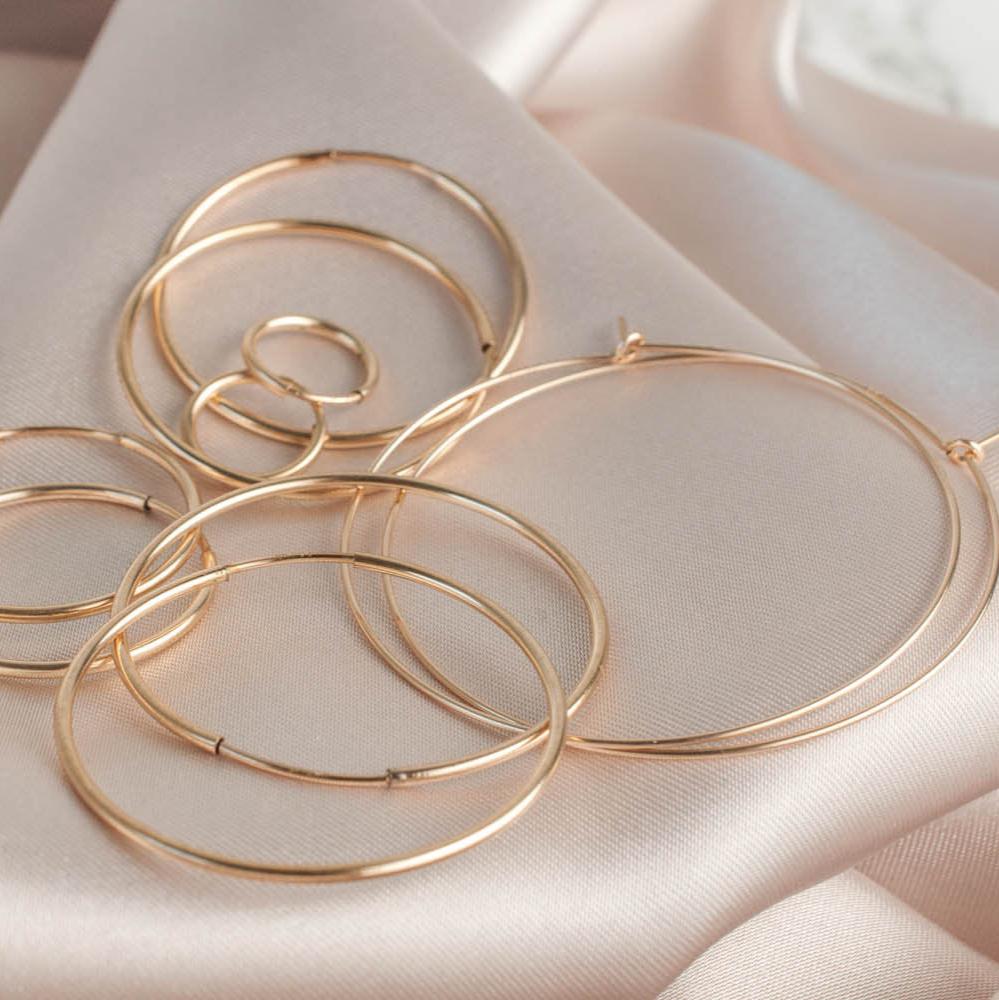 Stacked 14k gold filled Nia sleeper hoop earrings resting on champagne silk