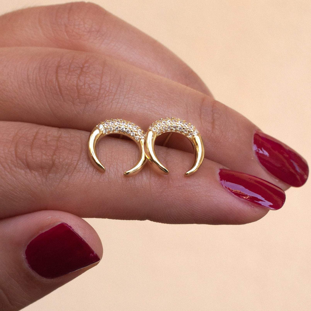 Woman holding pair of Bravi Double Horn 14k gold plated stud earrings between fingers