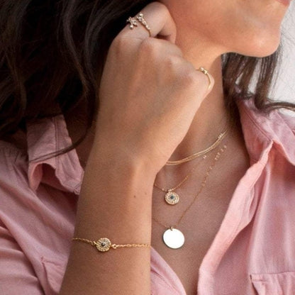 Woman wearing Elin Round Evil Eye 14k gold filled necklace layered with dainty chains in pink button-down shirt