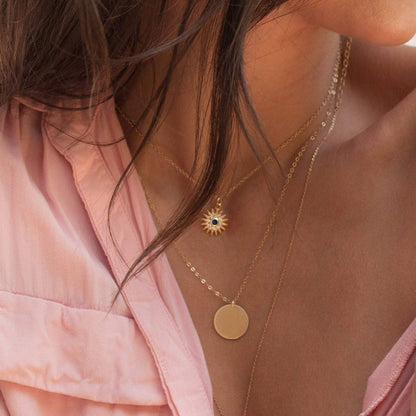 Woman wearing Sunniva Sun Ray & Starburst 14k gold filled necklace layered with coin pendant in unbuttoned pink shirt