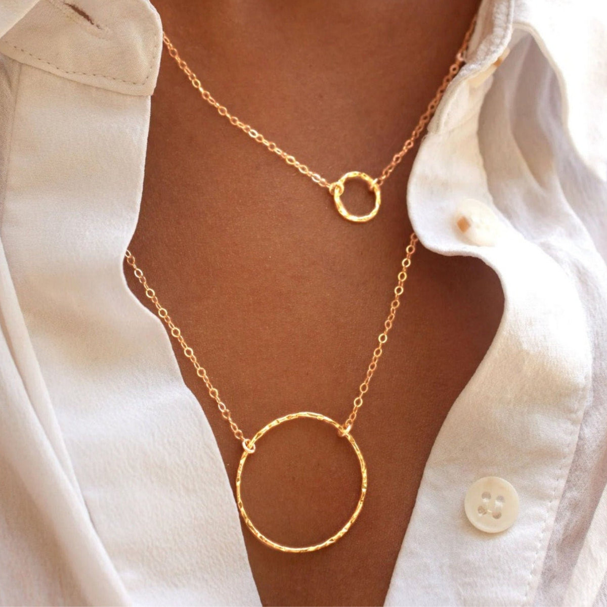 Woman wearing layered Sora Hammered Circle 14k gold vermeil necklaces in white button-down shirt