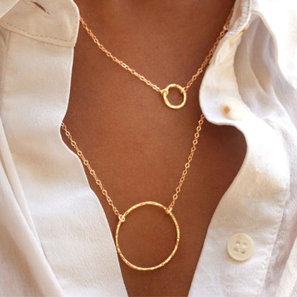 Woman wearing layered Sora Hammered Circle 14k gold vermeil necklaces in white button-down shirt