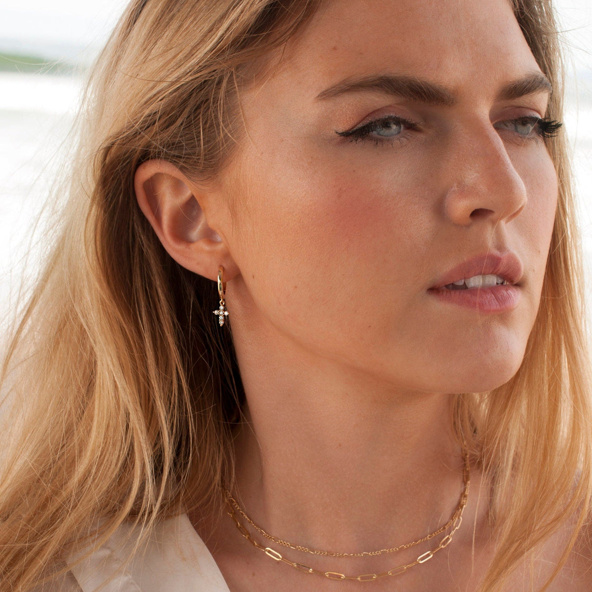 Woman with blonde hair looking away while wearing 14k Gold Plated Solid Mini Cross Hoops.