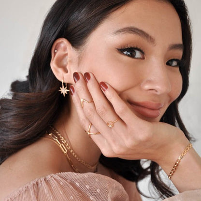 Woman with dark hair touching her cheek while smiling and wearing 14k Gold Plated Sola Starburst Earrings.
