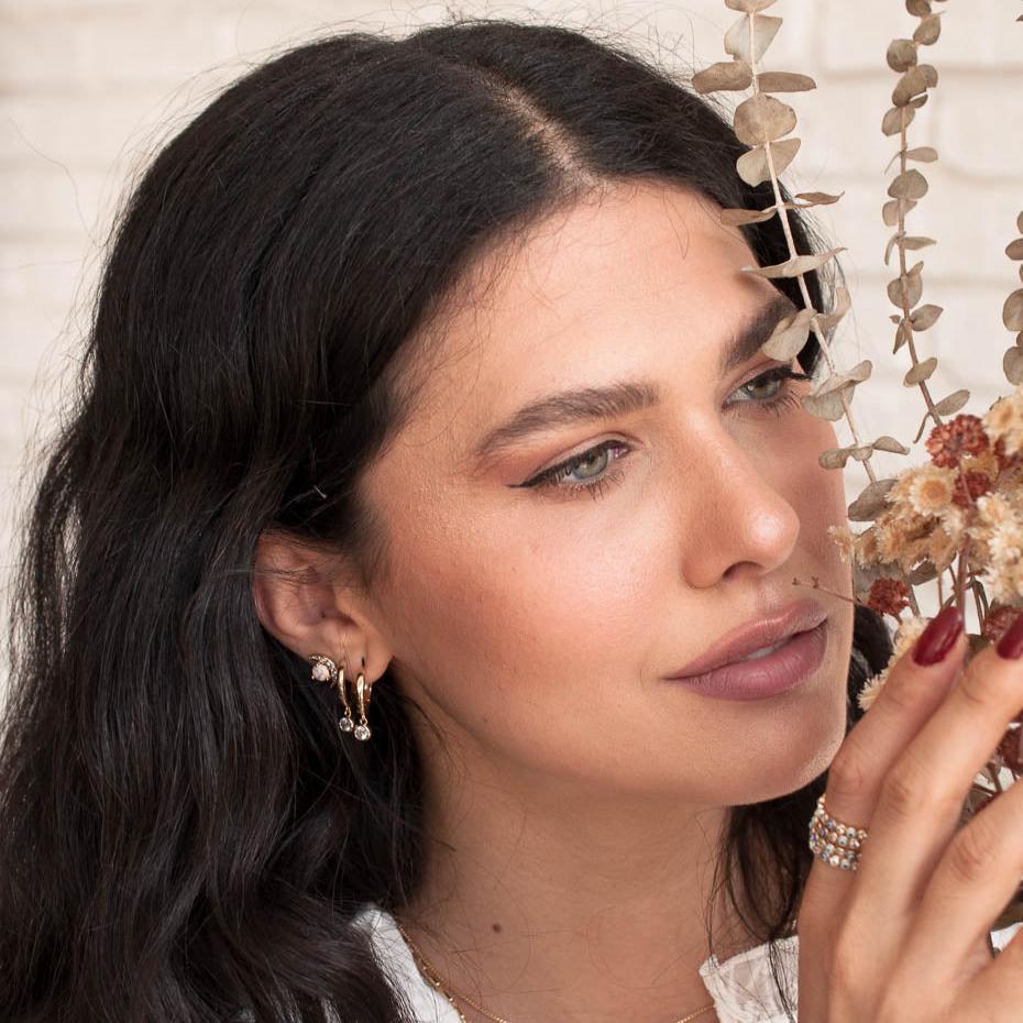 Woman with dark hair wearing 14k gold plated Lila solitaire crystal huggie drop earrings