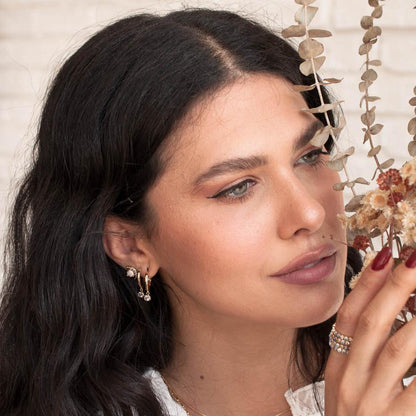 Woman with dark hair wearing 14k gold plated Lila solitaire crystal huggie drop earrings