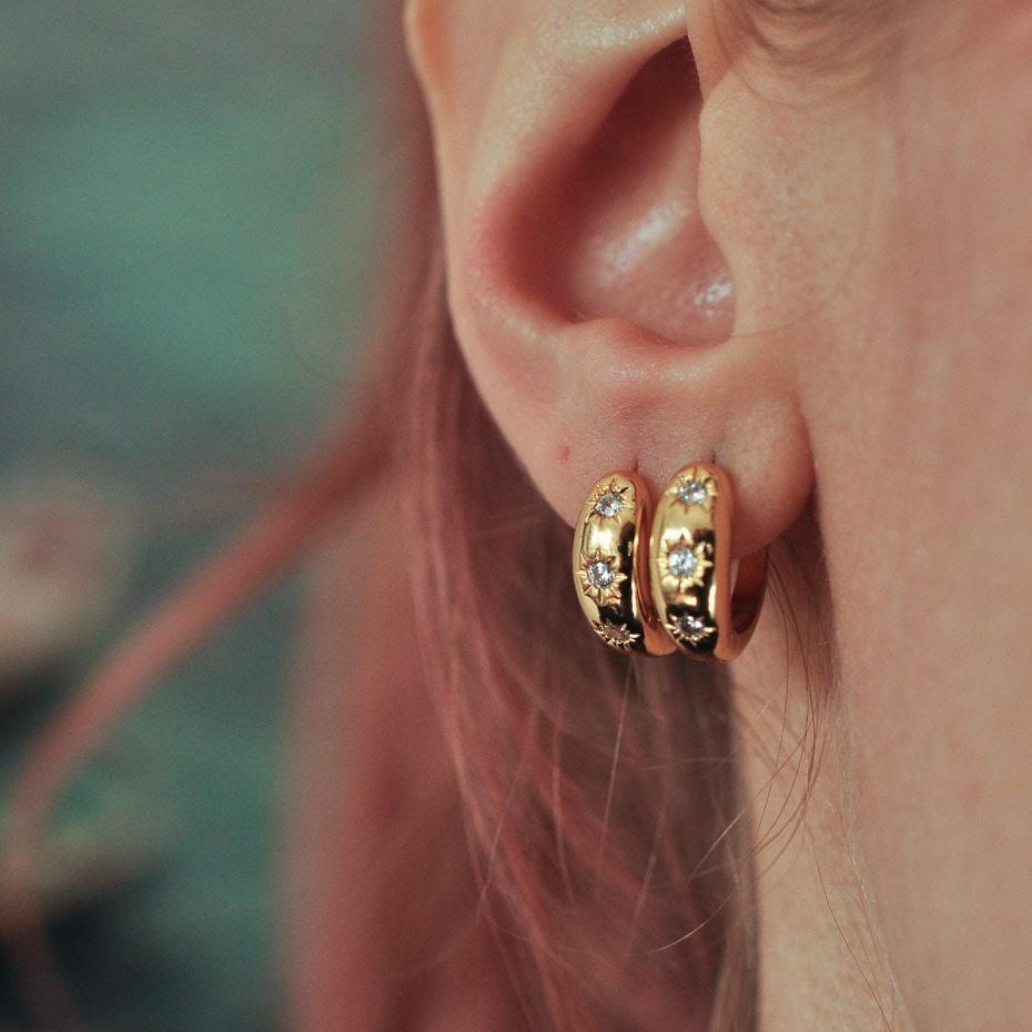 Woman with stacked lobe piercings wearing two 14k Gold Plated starburst crystal huggie hoop earrings.