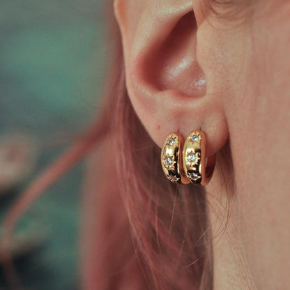 Woman with stacked lobe piercings wearing two 14k Gold Plated starburst crystal huggie hoop earrings.