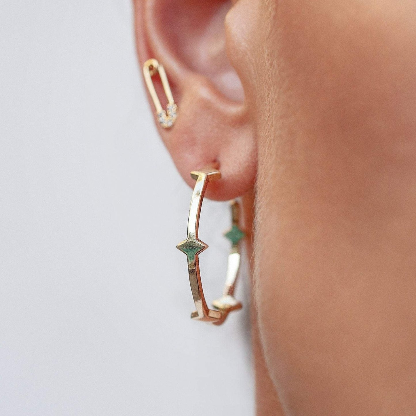 Statement Gold hoop earrings with spike and paperclip stud earring on woman's ear.
