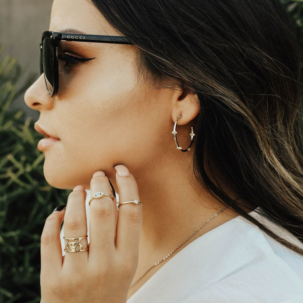Woman wearing gold statement hoop earrings with stacked rings and gucci sunglasses.