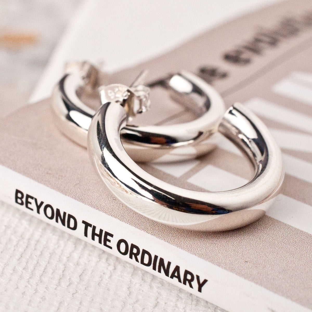 women's sterling silver chunky hoop earrings resting on a white book surface.