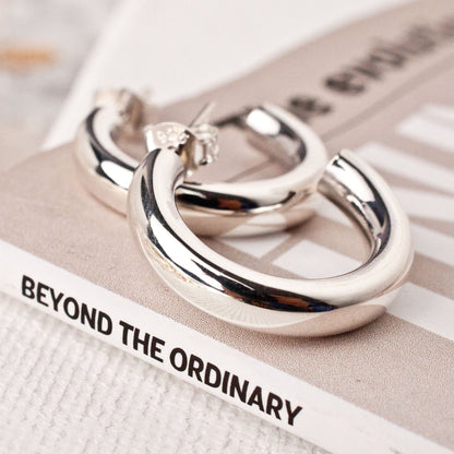 women's sterling silver chunky hoop earrings resting on a white book surface.
